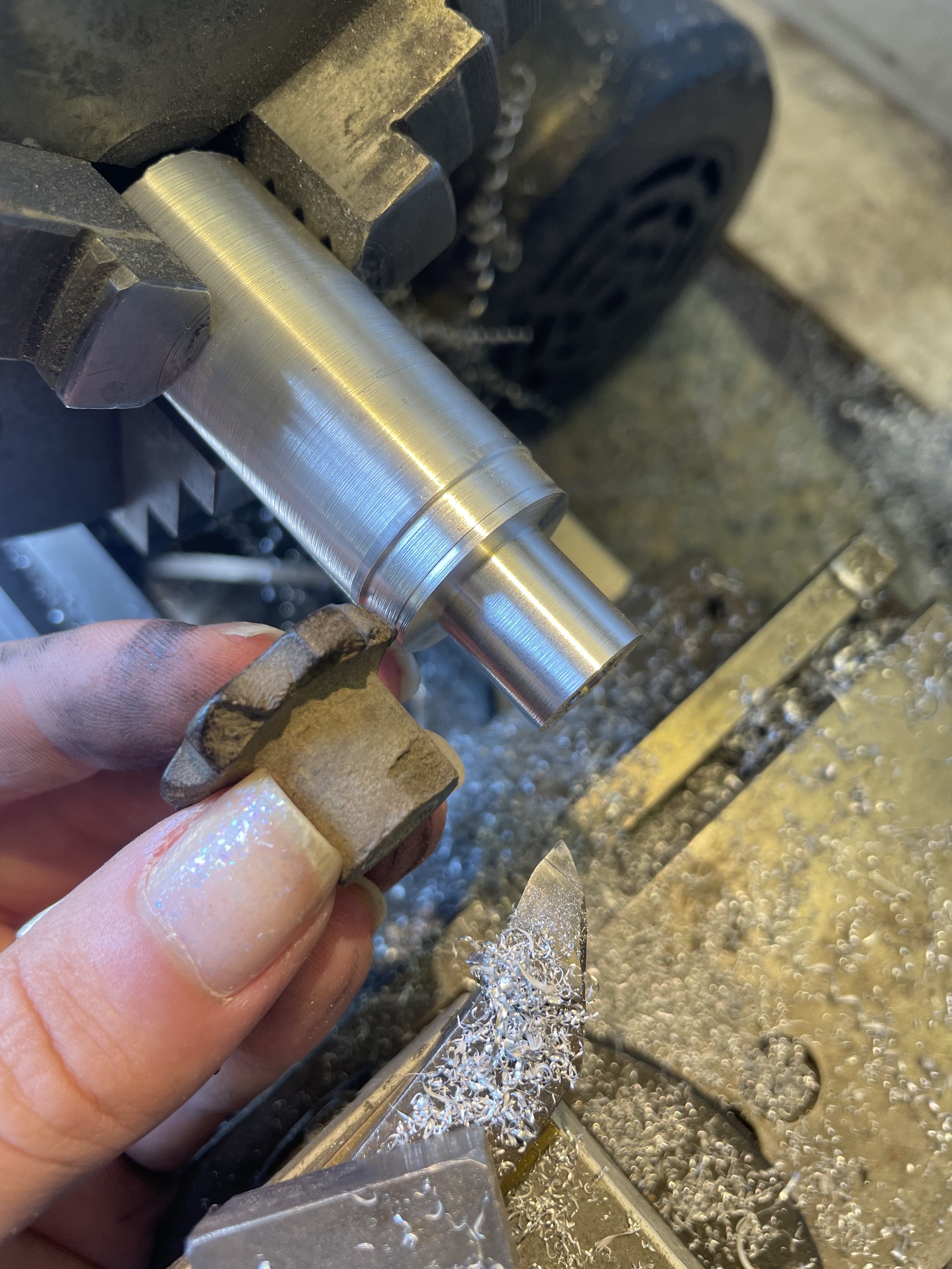 the original broken knob held next to a piece of aluminium in the chuck of a lathe