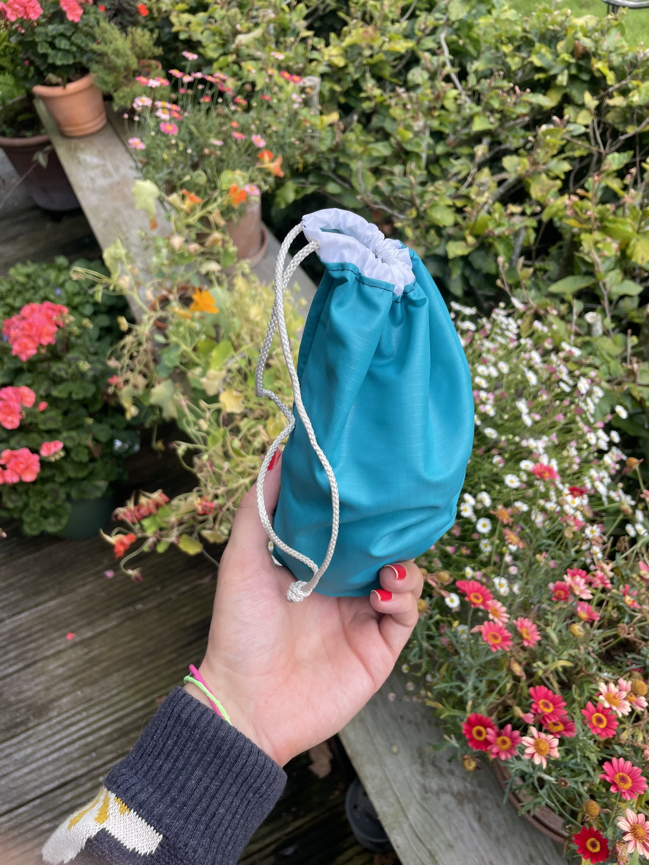 The pouch, closed. It is made of a turquoise tent fabric with a small white cord tube around the rim. In that tube, a white drawcord sits for pulling the pouch shut.