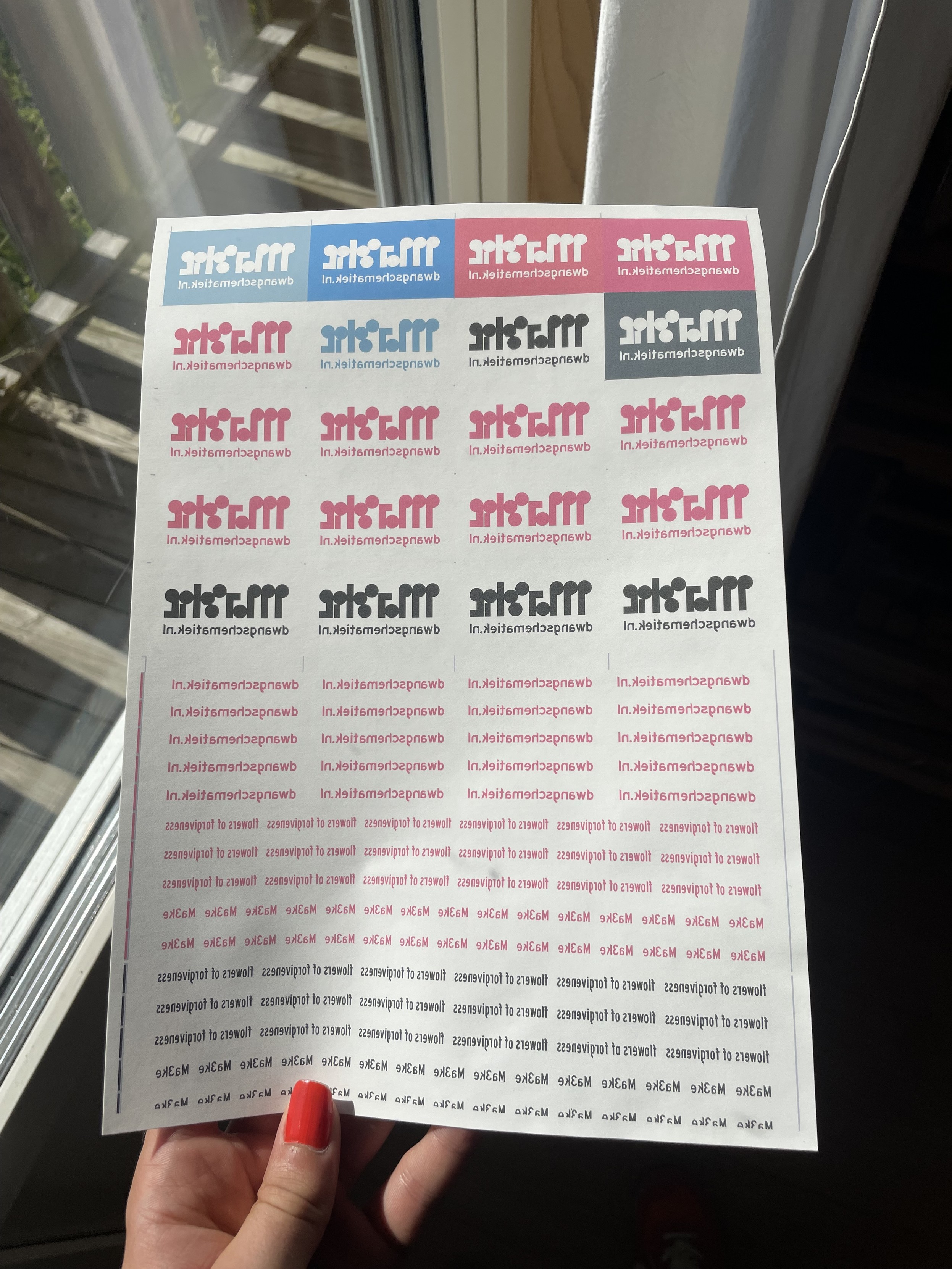 I hold up an A4 sheet of transfer paper printed with colorful labels. The printing is mirrored. 
