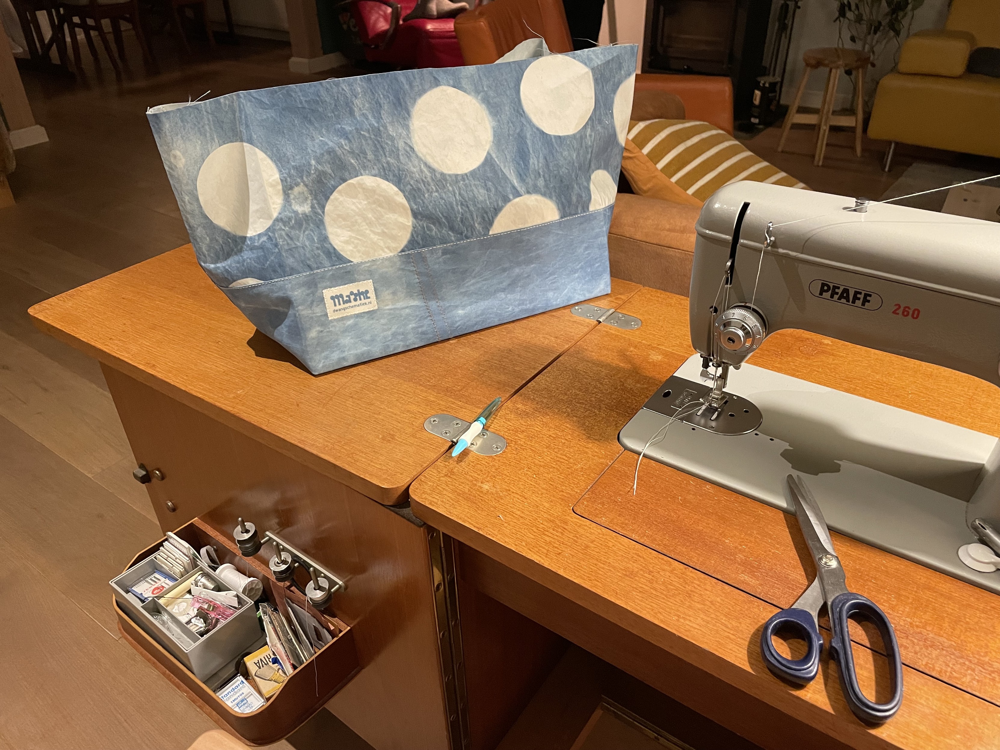 The lower part of a bag on my sewing machine table. The fabric is a nice grey-blue dyed sailcloth with large white dots on the upper section of the bag. 