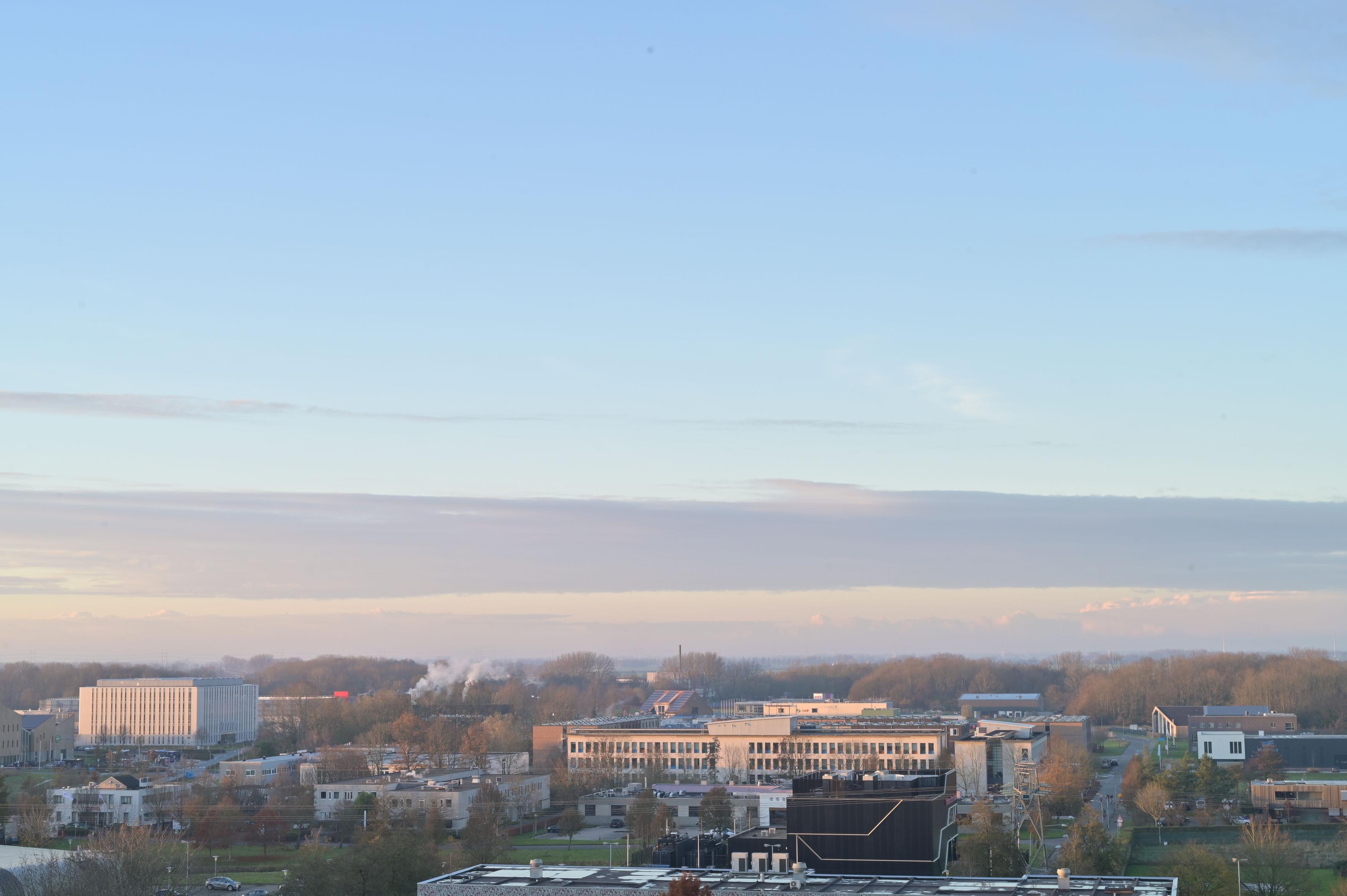 Sunlight with a slight orange tone hits buildings at a university campus. Beautiful sky with drawn cloud cover in the distance and clear skies right above.