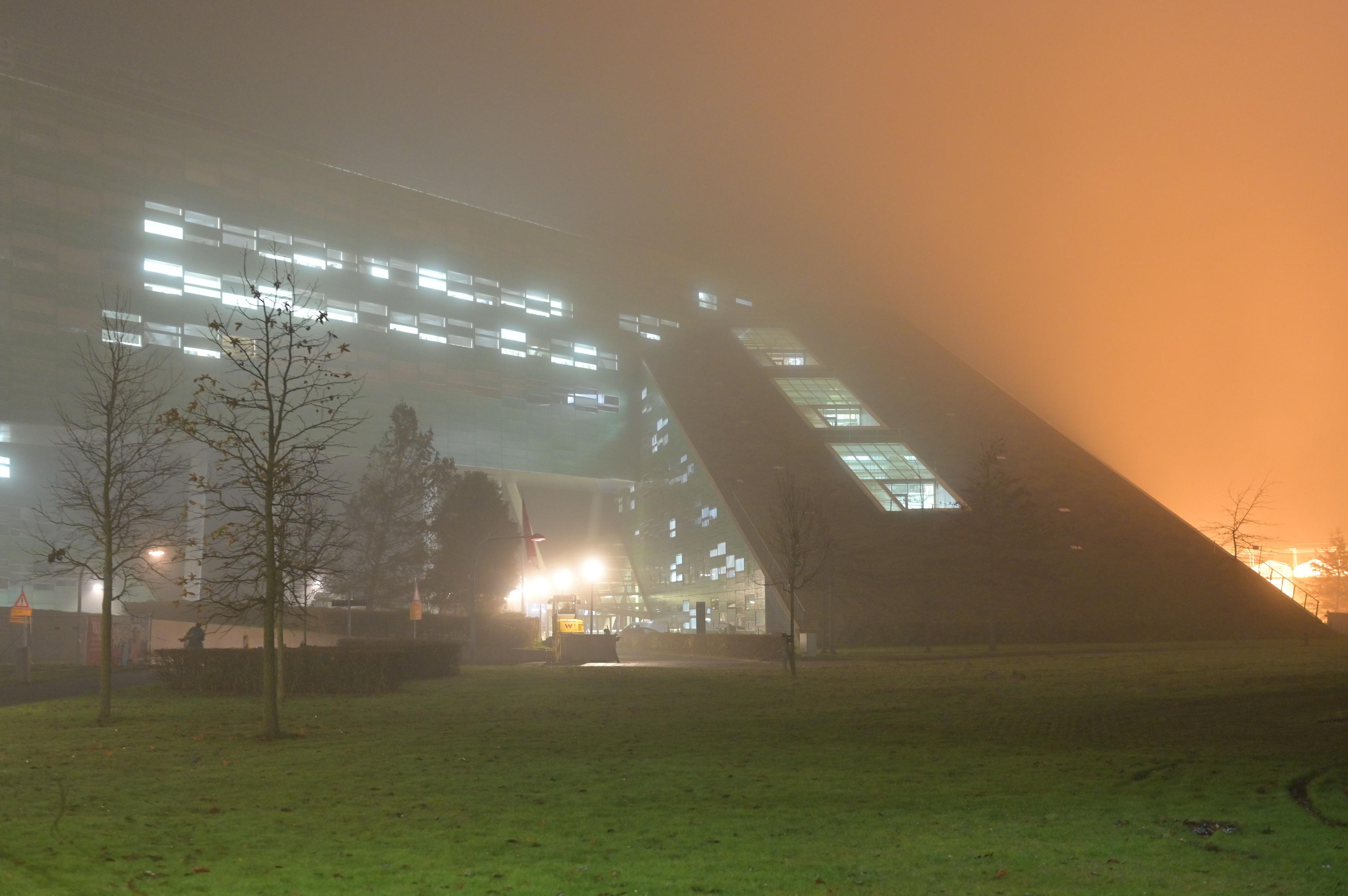 Thick fog illuminated by white light from a strange looking green building. This is where I work. Behind the building are some greenhouses for plant biology which produce very strong orange light filling an entire third of the photograph as it is dispersed by the fog.