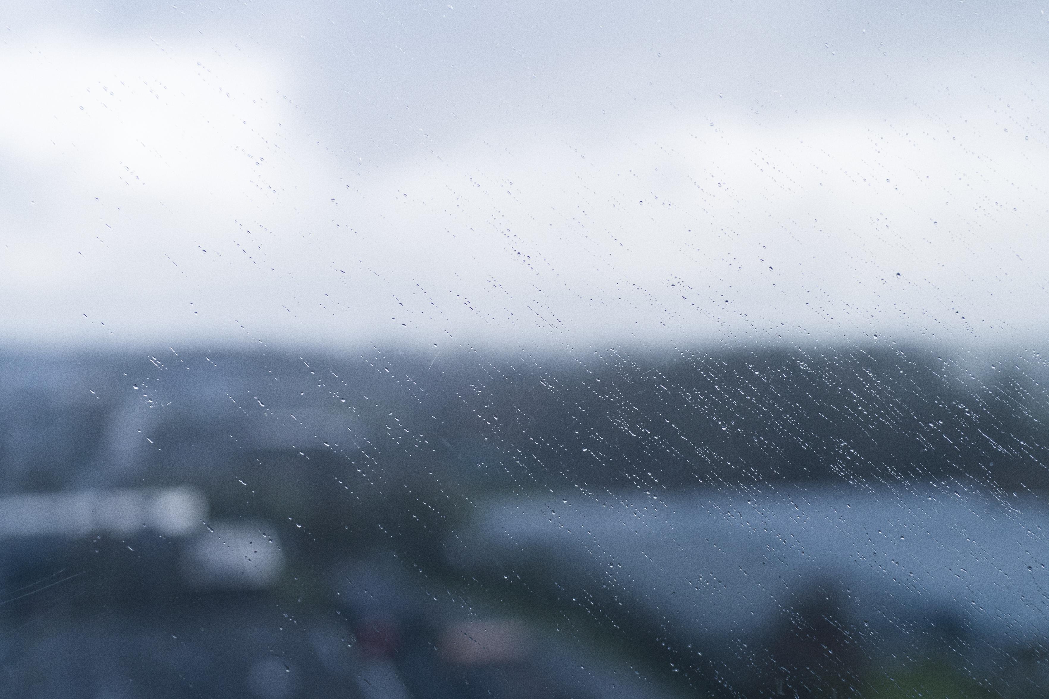 Raindrops form diagonal streaks on a window, with the world behind it very blurry and out of focus.