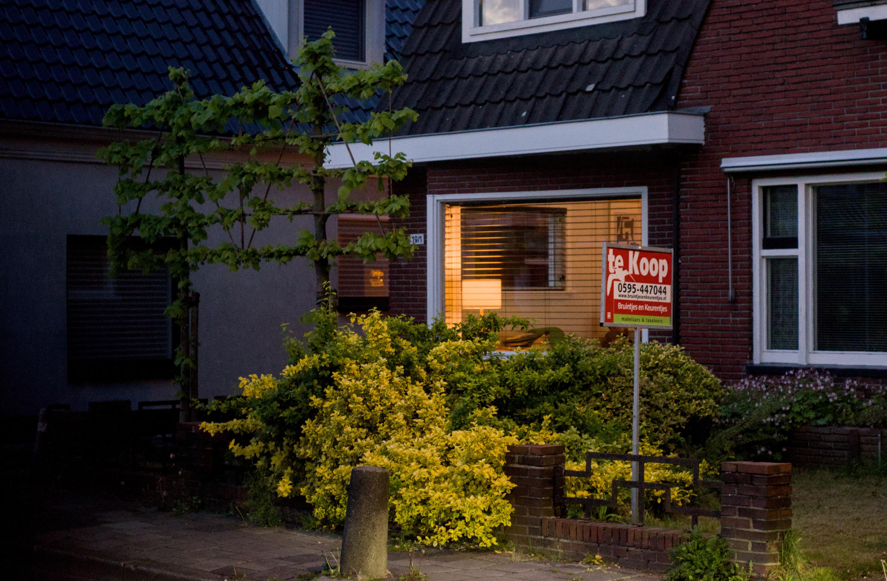 A house in dusk with warm light from the living room hitting a ligth-green bush in its front garden.