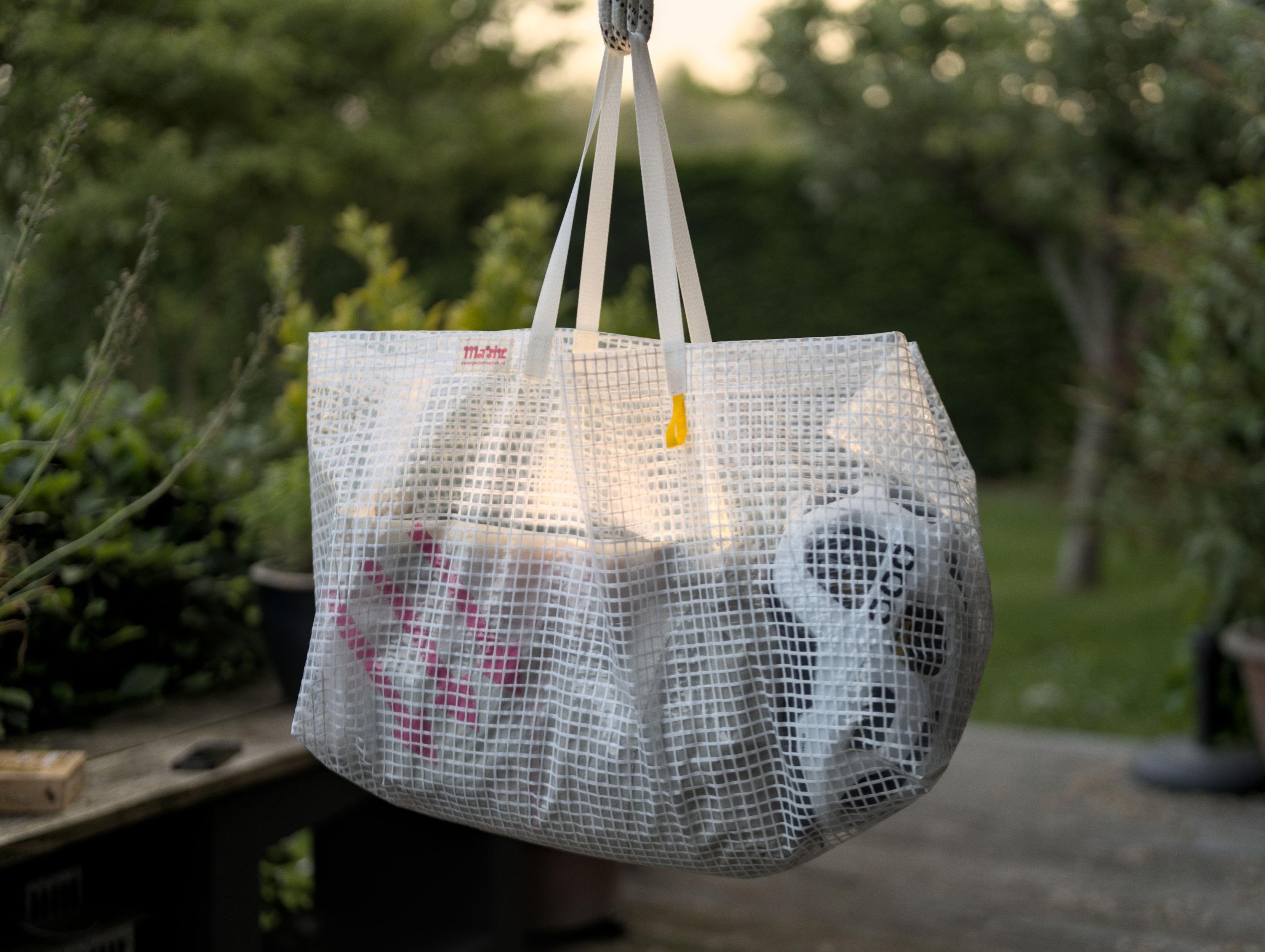 A large bag made of a transparent material fortified
			  with white fibers hangs on a rope in a garden. You
			  can see my backpack and bike helmet through the walls
			  of the bag. On the top rim are my label and a yellow
			  loop is attached right under the handles. The handles
			  are made of a white webbing. I placed a lamp inside
			  the bag to make the photo look cool. As a result,
			  this photo looks extremely cool.