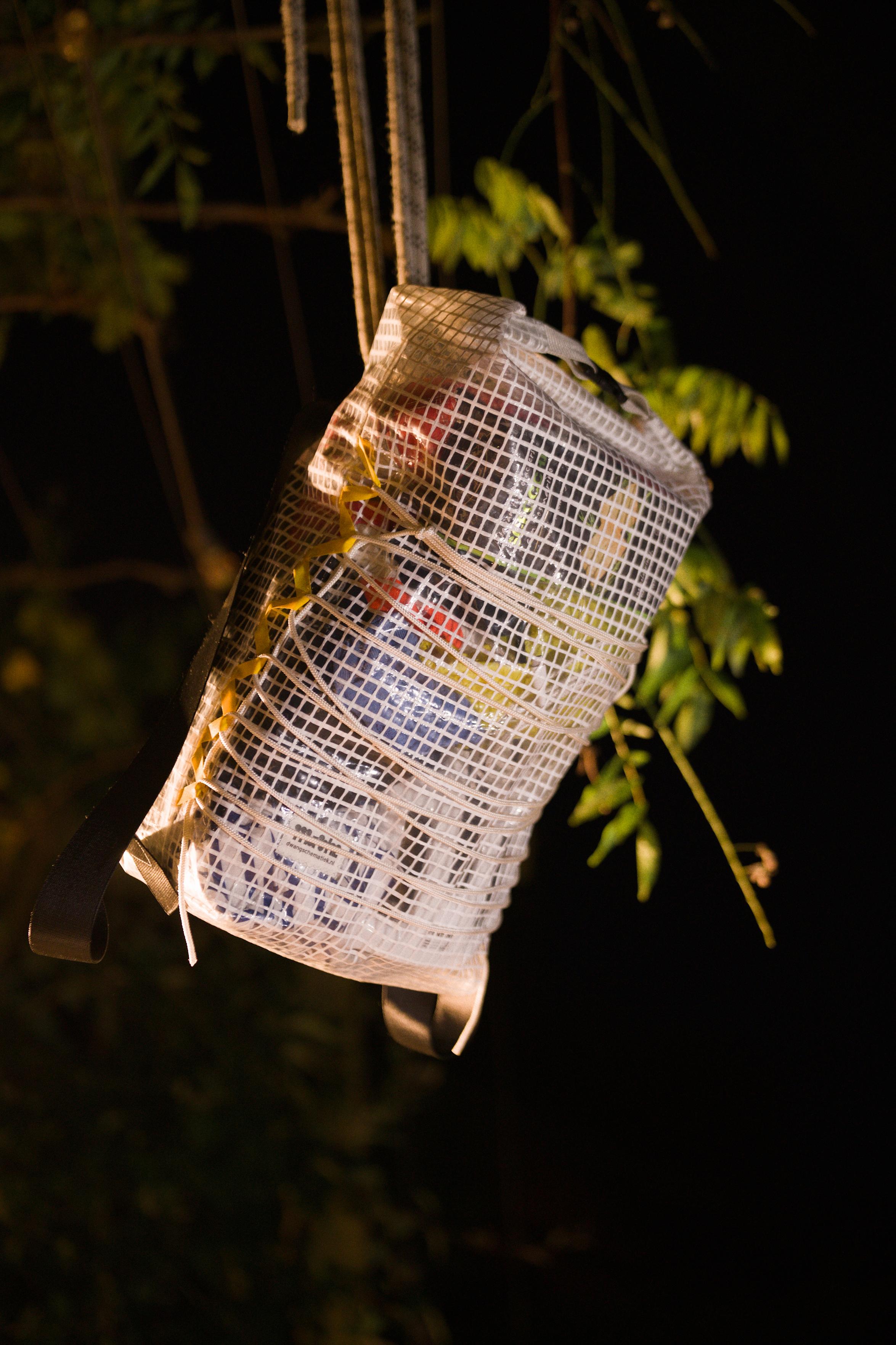 The backpack hangs on a rope next to some plant vines.